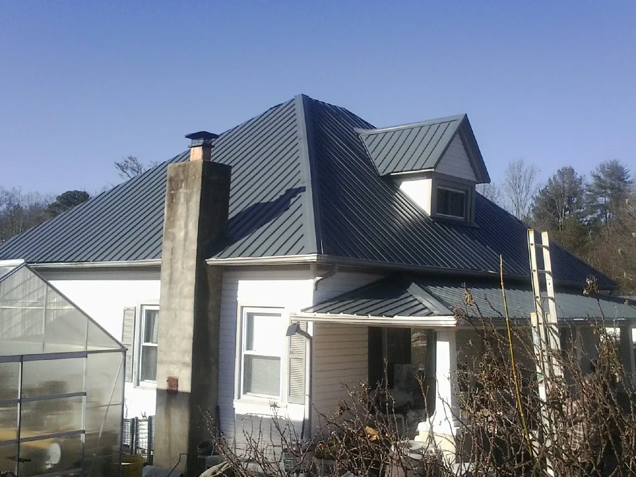 Dark blue standing seam metal roof on a white farmhouse with dormer — Slate & Tile Roof Repair by Roofing Brothers in North Las Vegas