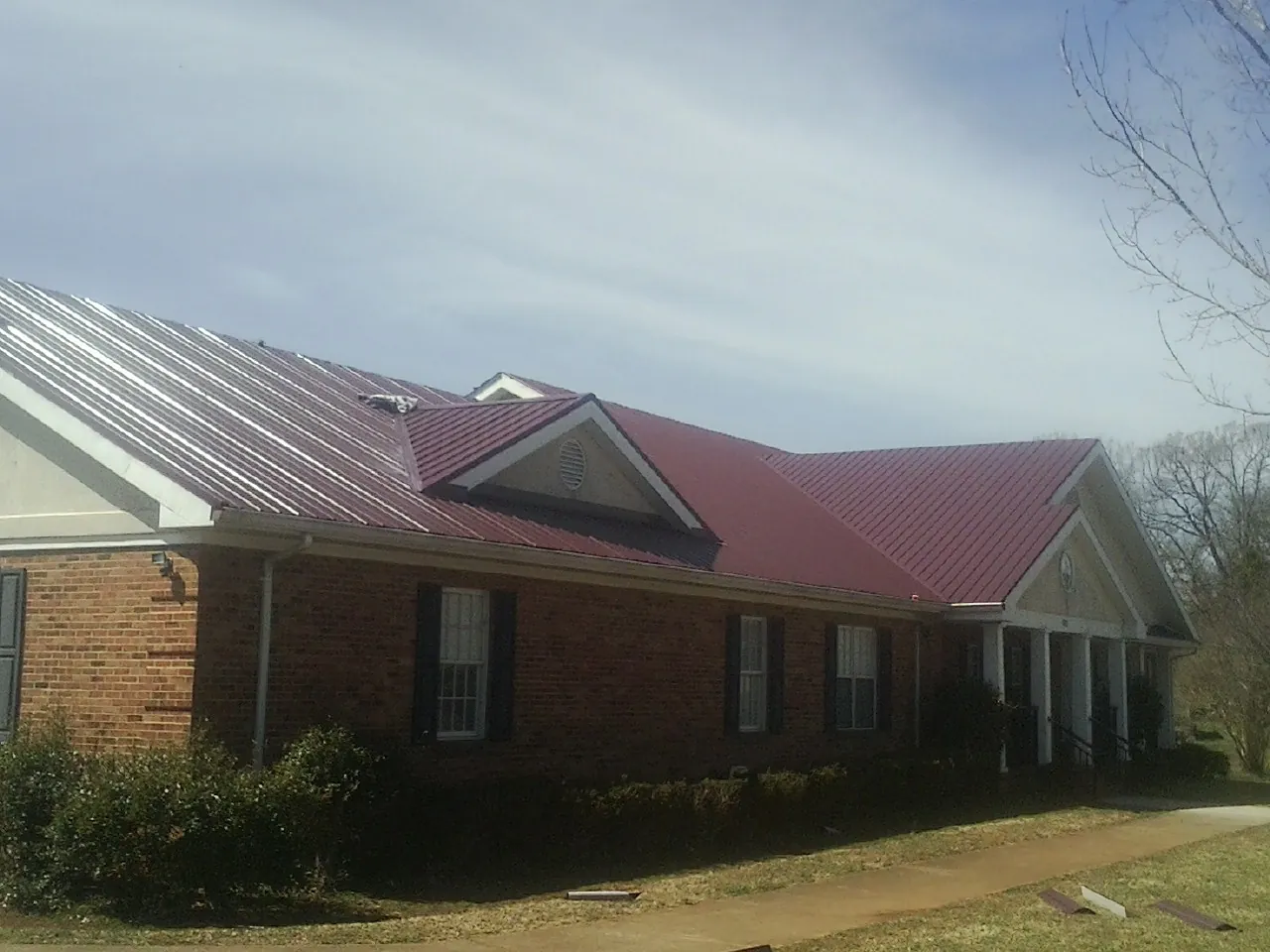 Red metal roof with gabled entries on a long brick building, from a Hail Damage Roof Repair job in North Las Vegas