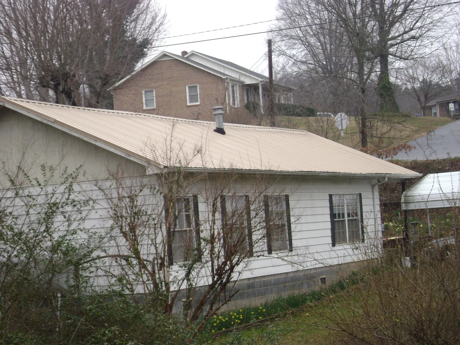 Tan metal roof on a white sided house set into a hillside — Commercial Roofing by Roofing Brothers in North Las Vegas